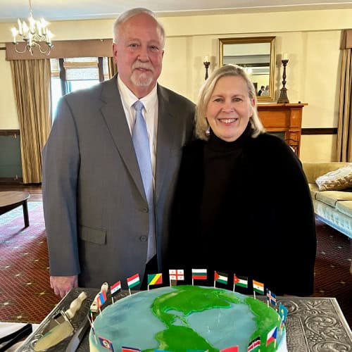 A man and woman stand indoors behind a cake with a world map at a Baton Rouge Presbyterian Church event.