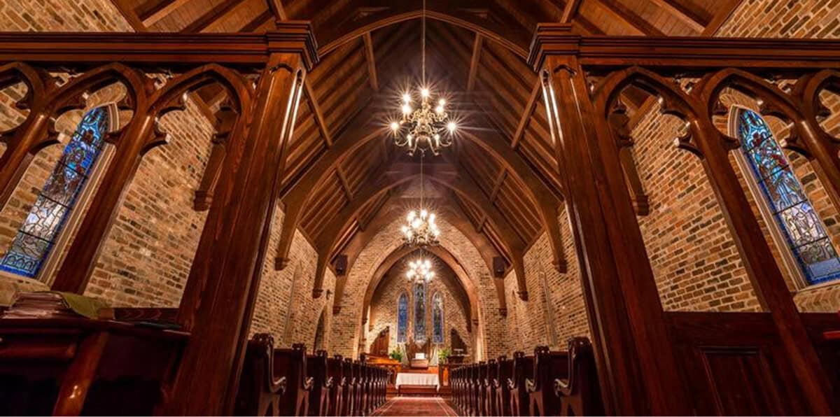 Interior of First Presbyterian Baton Rouge, featuring wooden pews, vaulted ceiling, brick walls, chandeliers, and stained glass windows.