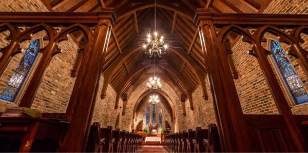 Interior of First Presbyterian Baton Rouge, featuring wooden pews, vaulted ceiling, brick walls, chandeliers, and stained glass windows.