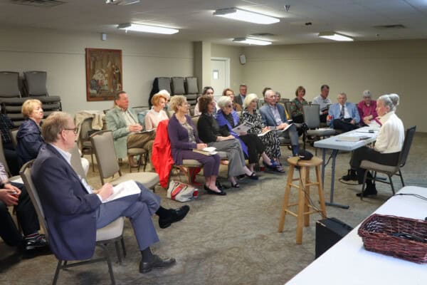 A group attends a meeting at First Presbyterian Baton Rouge, seated around a table, listening attentively with papers and chairs visible.