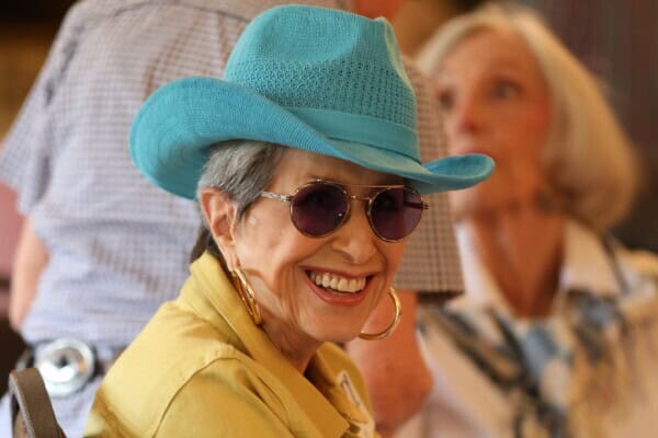 An older woman in a blue cowboy hat smiles at the camera, attending first presbyterian baton rouge as someone stands out of focus behind her.
