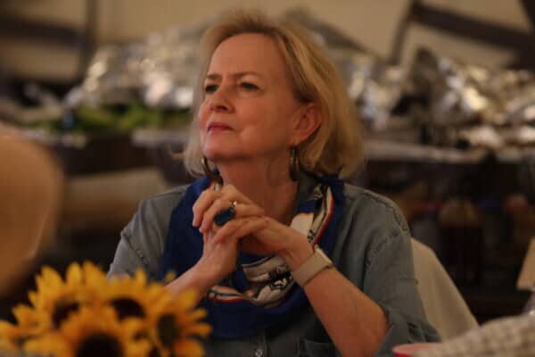 A woman with short blonde hair sits at a table, sunflowers in front, at Baton Rouge Presbyterian Church.