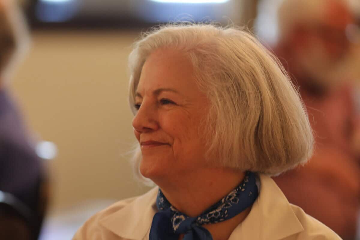 An older woman with gray hair and a blue scarf smiles while looking to the side at Baton Rouge Presbyterian Church services.