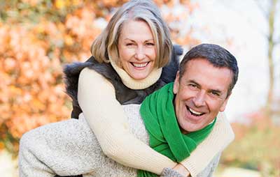 Older woman smiles giving a piggyback ride to an older man in a green scarf, enjoying autumn near First Presbyterian Baton Rouge.