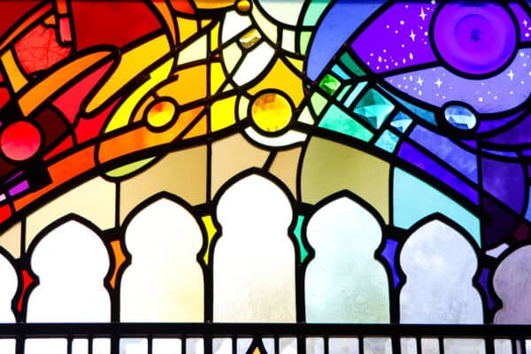 Colorful stained glass window with geometric patterns and arches, featuring shades of red, yellow, green, blue, and purple.