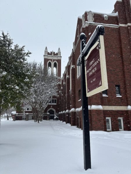 A red brick church with a tower and First Presbyterian Baton Rouge sign, surrounded by snow-covered ground and trees.
