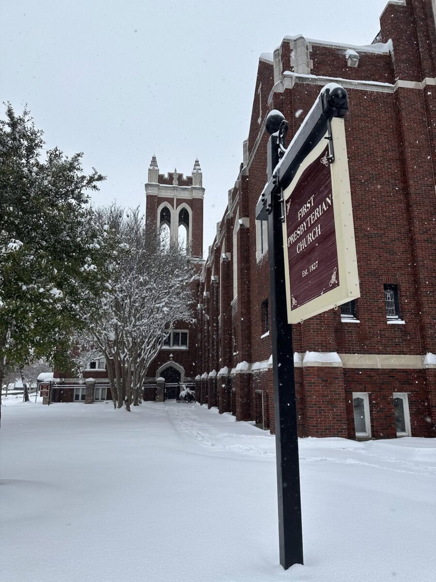 A red brick church with a tower and First Presbyterian Baton Rouge sign, surrounded by snow-covered ground and trees.