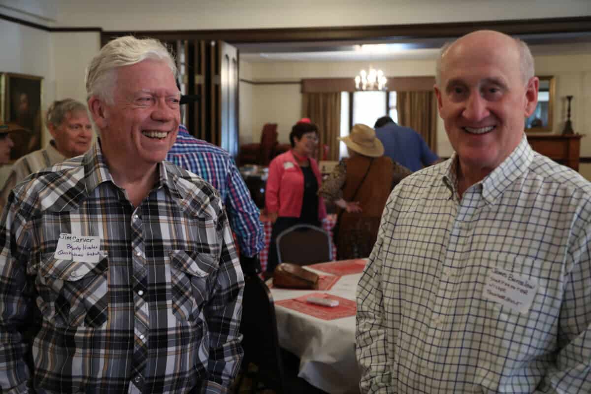Two older men in plaid shirts smile at a Baton Rouge Presbyterian Church gathering with others in the background.