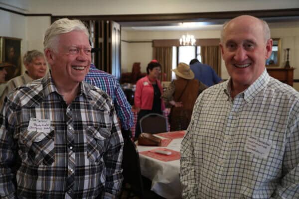 Two older men in plaid shirts smile at a Baton Rouge Presbyterian Church gathering with others in the background.