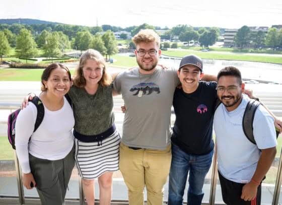 Five people stand arm in arm outdoors at First Presbyterian Baton Rouge, smiling with grass and buildings in the background.