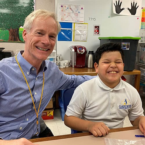 An adult and a child sit smiling at a classroom table at First Presbyterian Baton Rouge, with supplies and artwork in the background.