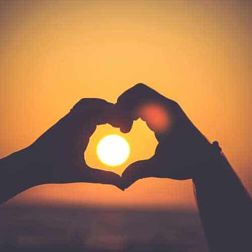 Two hands form a heart shape framing the setting sun, with an orange sky behind—capturing warmth at Baton Rouge Presbyterian Church.