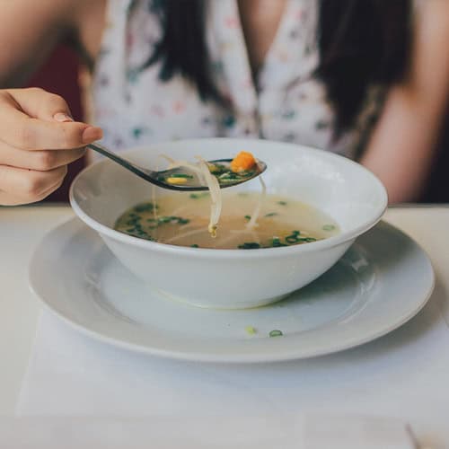 A person enjoys noodle soup above a white bowl, seated at a table near First Presbyterian Baton Rouge.
