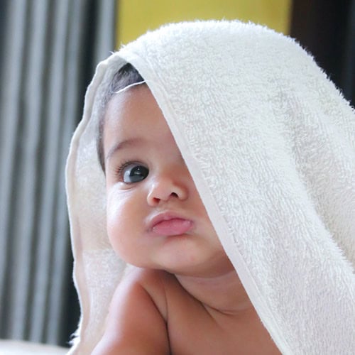 A baby with a white towel draped over their head looks forward with a slightly puckered expression at First Presbyterian Baton Rouge.