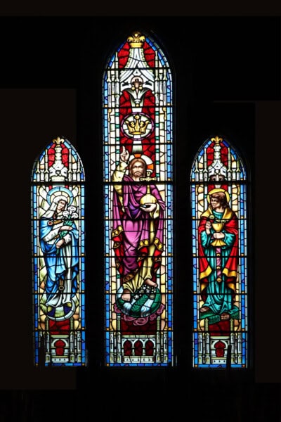 Three stained glass windows depicting religious figures, each with symbolic items, set against a dark background.