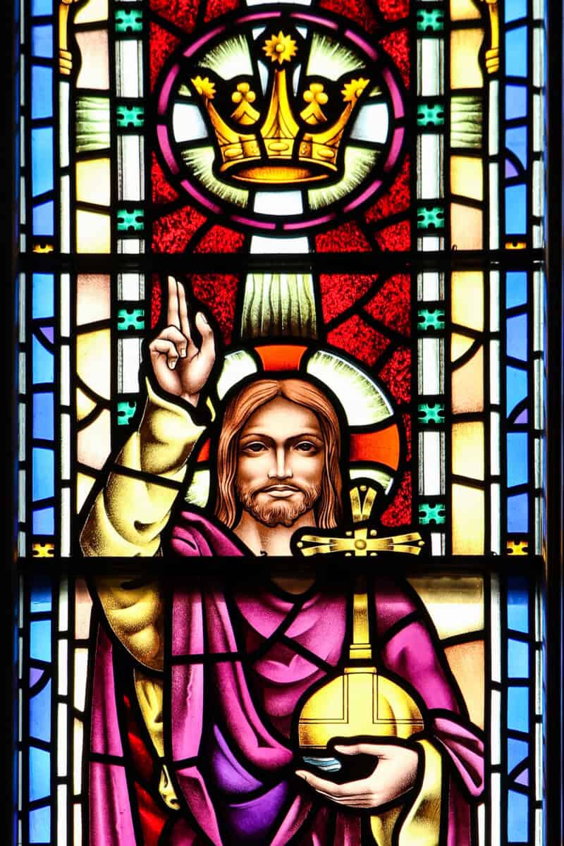 Stained glass window at First Presbyterian Baton Rouge shows a haloed figure with raised hand, gold orb, and crown above their head.
