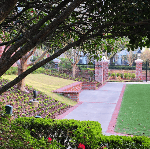 A landscaped garden shaped by customer feedback, with trimmed hedges, brick walls, paved paths, and trees partially shading the view.