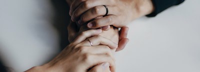 Four hands, two with rings, gently clasp together on a light surface, evoking comfort found at First Presbyterian Baton Rouge.