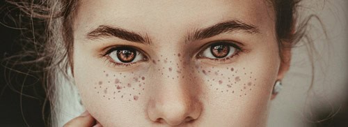 Close-up of a person's face with brown eyes, natural eyebrows, freckles, and reflecting the warmth of Baton Rouge Presbyterian Church.