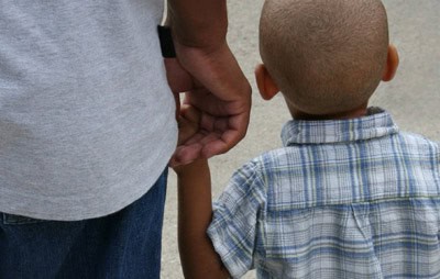 An adult and child, seen from behind, hold hands while walking—perhaps heading to First Presbyterian Baton Rouge for church services.