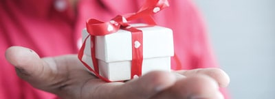 A person holds a small white gift box with a red ribbon, perfect for First Presbyterian Baton Rouge celebrations, against a blurred background.
