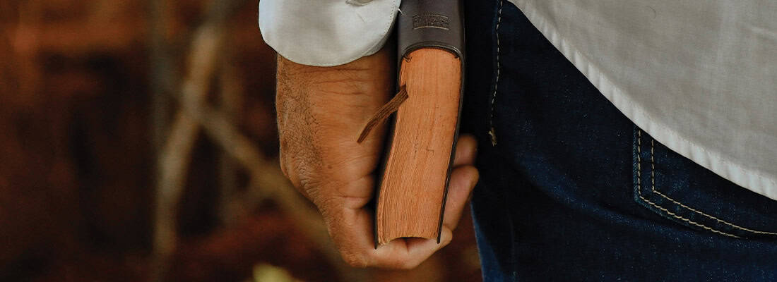 A person wearing jeans and a white shirt holds a closed book with a bookmark, near First Presbyterian Baton Rouge.