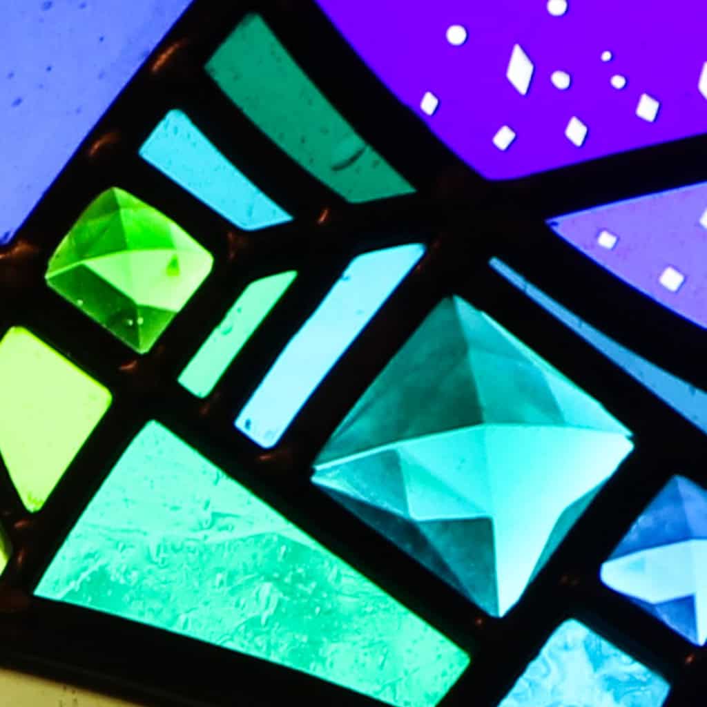 Close-up of a stained glass window at First Presbyterian Baton Rouge, featuring blue, green, and purple geometric shapes divided by black metal lines.