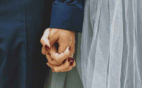 Two people hold hands, one in dark and one in tulle-like fabric, their rings shining—a moment from a Connection Couples' Workshop.