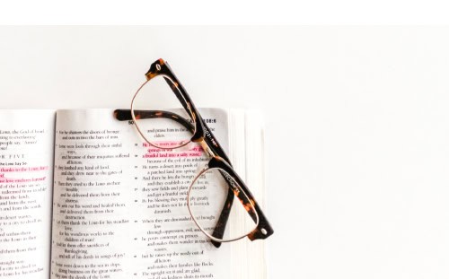 A pair of tortoiseshell eyeglasses rests on an open book with a passage on Elder Election highlighted in pink.