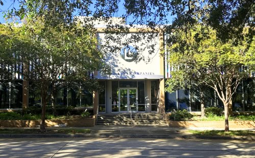 A modern office building with large windows and a main entrance, surrounded by trees, just as it was done for us with landscaped greenery.