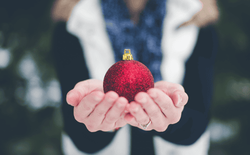 Person holding a red glittery Christmas ornament with both hands, outdoors—perfect for Christmas bags or Malachi Dads donations.
