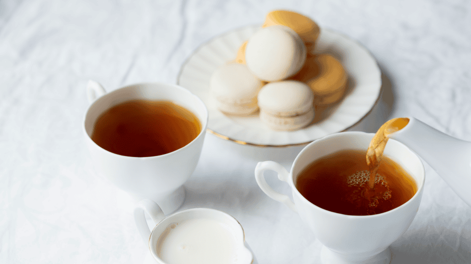Two cups of tea, milk, and assorted macarons set for a delightful Advent Tea on a crisp white tablecloth.