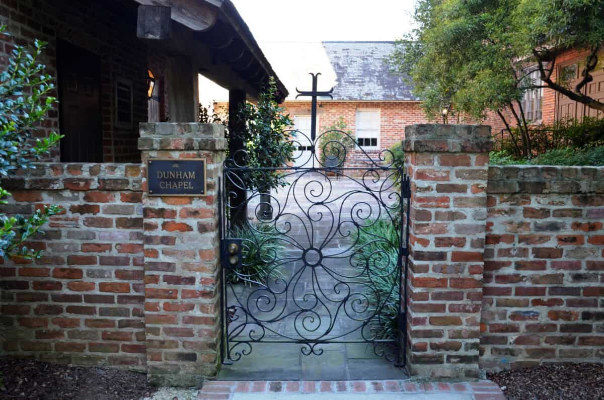 A black wrought iron gate opens into a brick courtyard with a sign reading "Dunham Chapel" on the left brick column.
