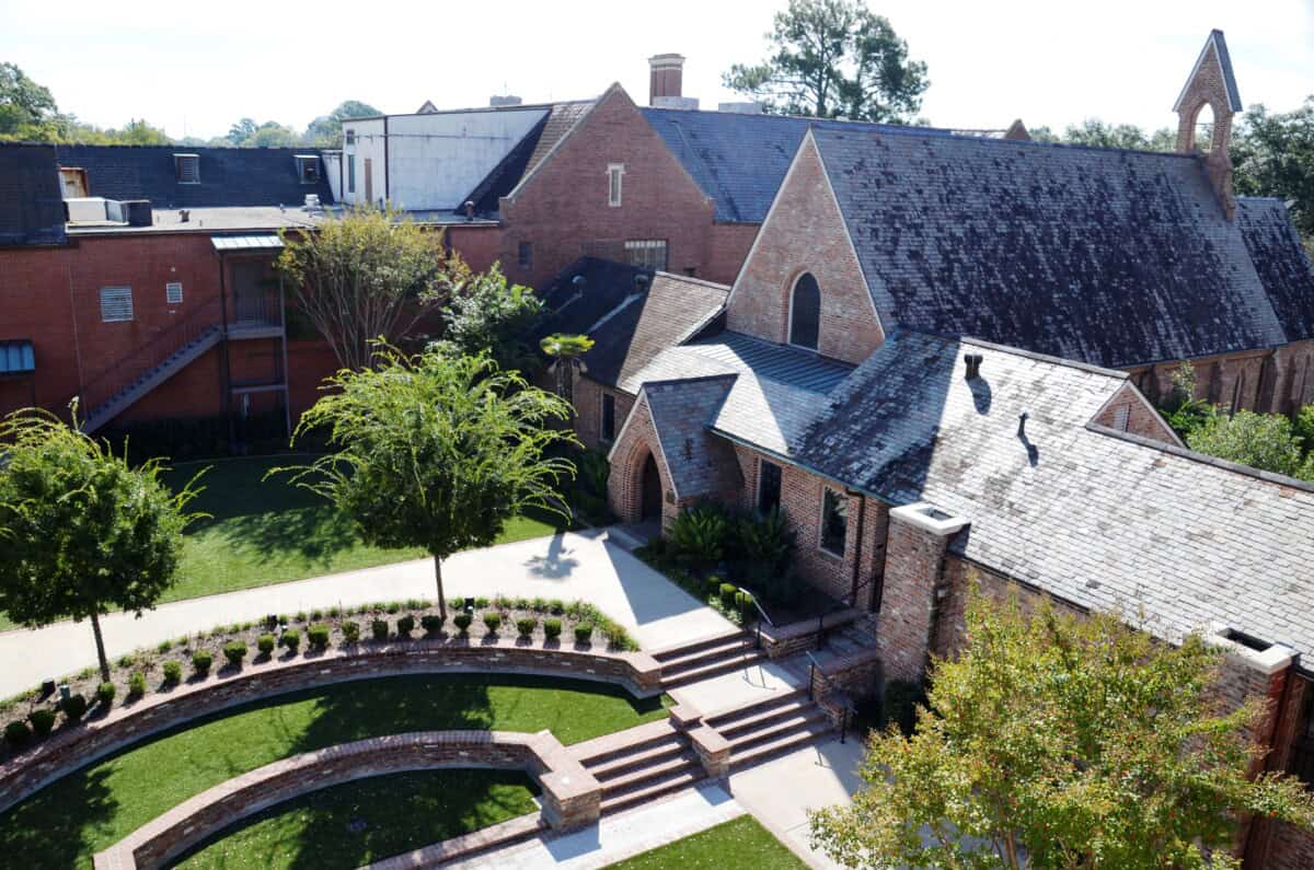 A brick church with arched windows and steep roof sits next to a curved walkway and neatly landscaped green lawn.