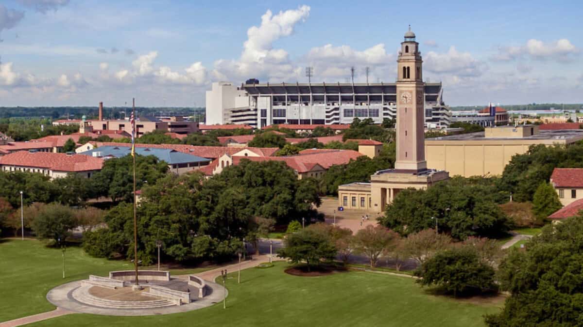 A campus landscape with a clock tower, trees, and the LSU Prayer Walk near First Presbyterian under a partly cloudy sky.
