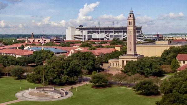 A campus landscape with a clock tower, trees, and the LSU Prayer Walk near First Presbyterian under a partly cloudy sky.