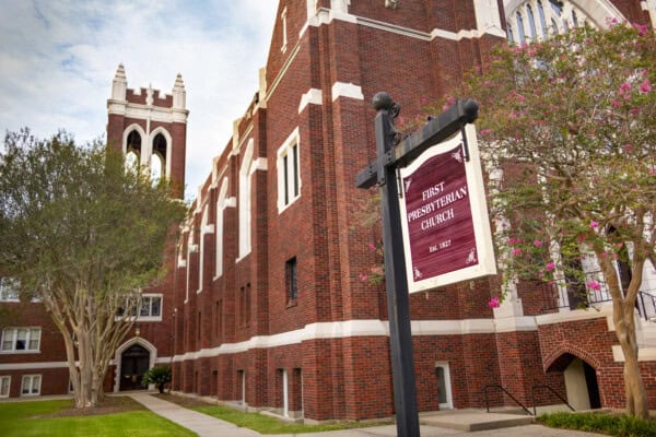 A red-brick church building with a tall tower stands near blooming trees, just across from the Block Library.