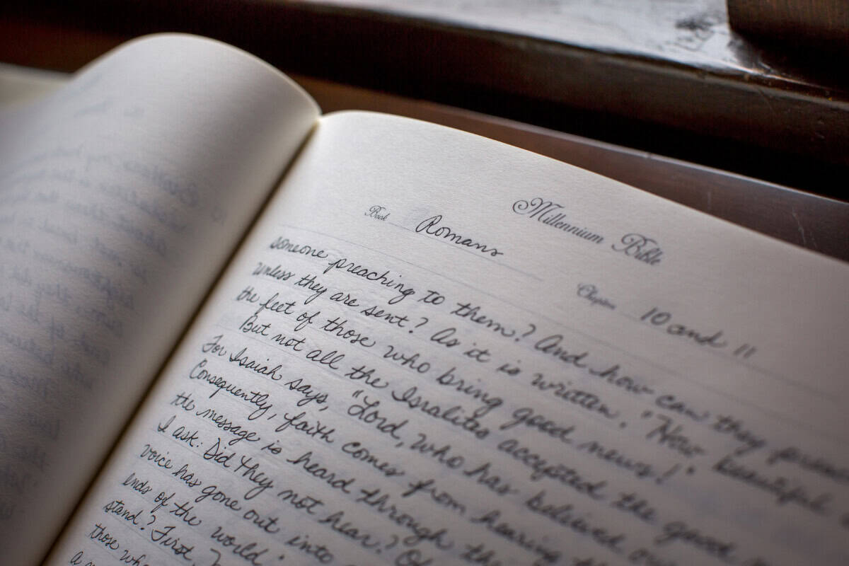 An open notebook from Block Library displays handwritten biblical text, with the heading "Romans" in neat cursive on lined pages.