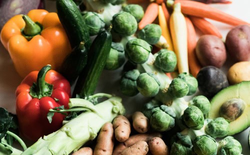 A variety of fresh vegetables sourced through local mission volunteer opportunities, including bell peppers, Brussels sprouts, and an avocado.