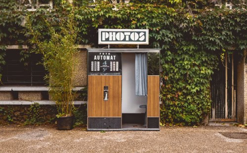 Outdoor vintage photo booth with "PHOTOS" sign, wood paneling, and curtain—join our photo contest for a chance to win prizes!.