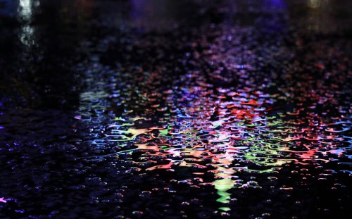 Colorful neon lights reflected on wet pavement—what will it be like to witness this blurry, abstract visual effect at night?.